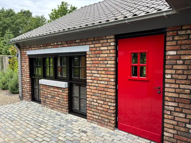 Bakstenen woning met zwart geschilderde kozijnen en een rode voordeur