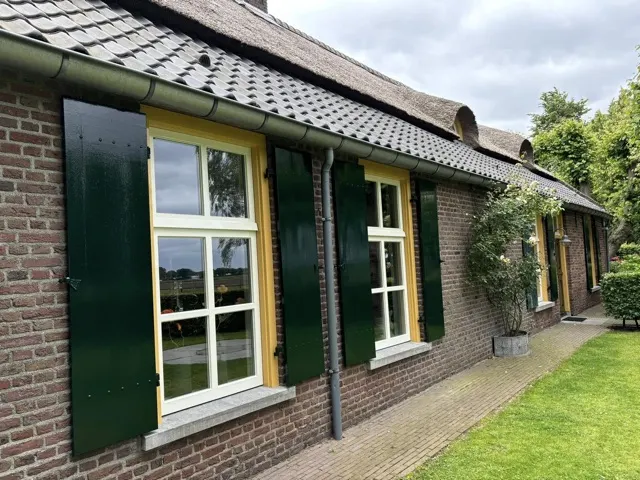 Woonboerderij met donkergroene luiken en gele kozijnen