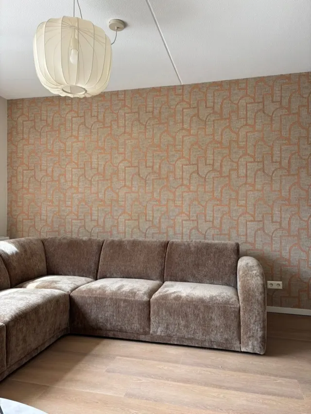 Woonkamer met beige geometrisch behang achter een hoekbank