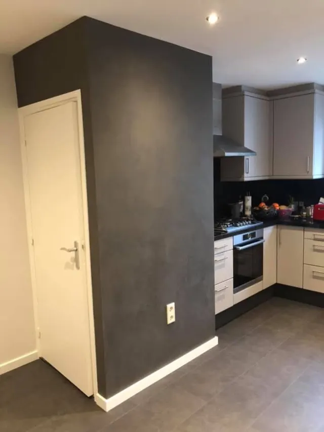 Donkergrijze betonlook scheidingswand naast een keuken