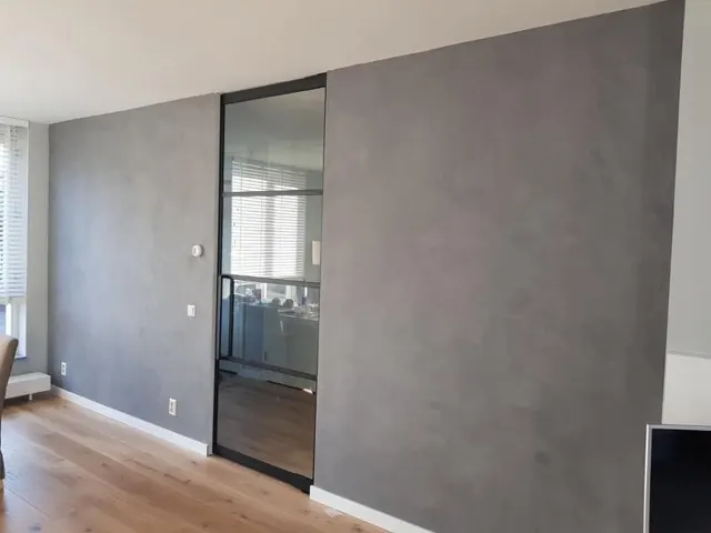 Grijze betonlook woonkamermuur met zwarte glazen deur